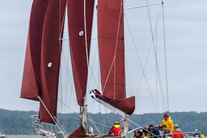 Sailboat with red sails and a group of people on board, sailing in cloudy weather.