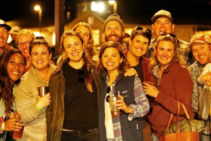 Group of smiling people posing outdoors at night, some holding drinks.